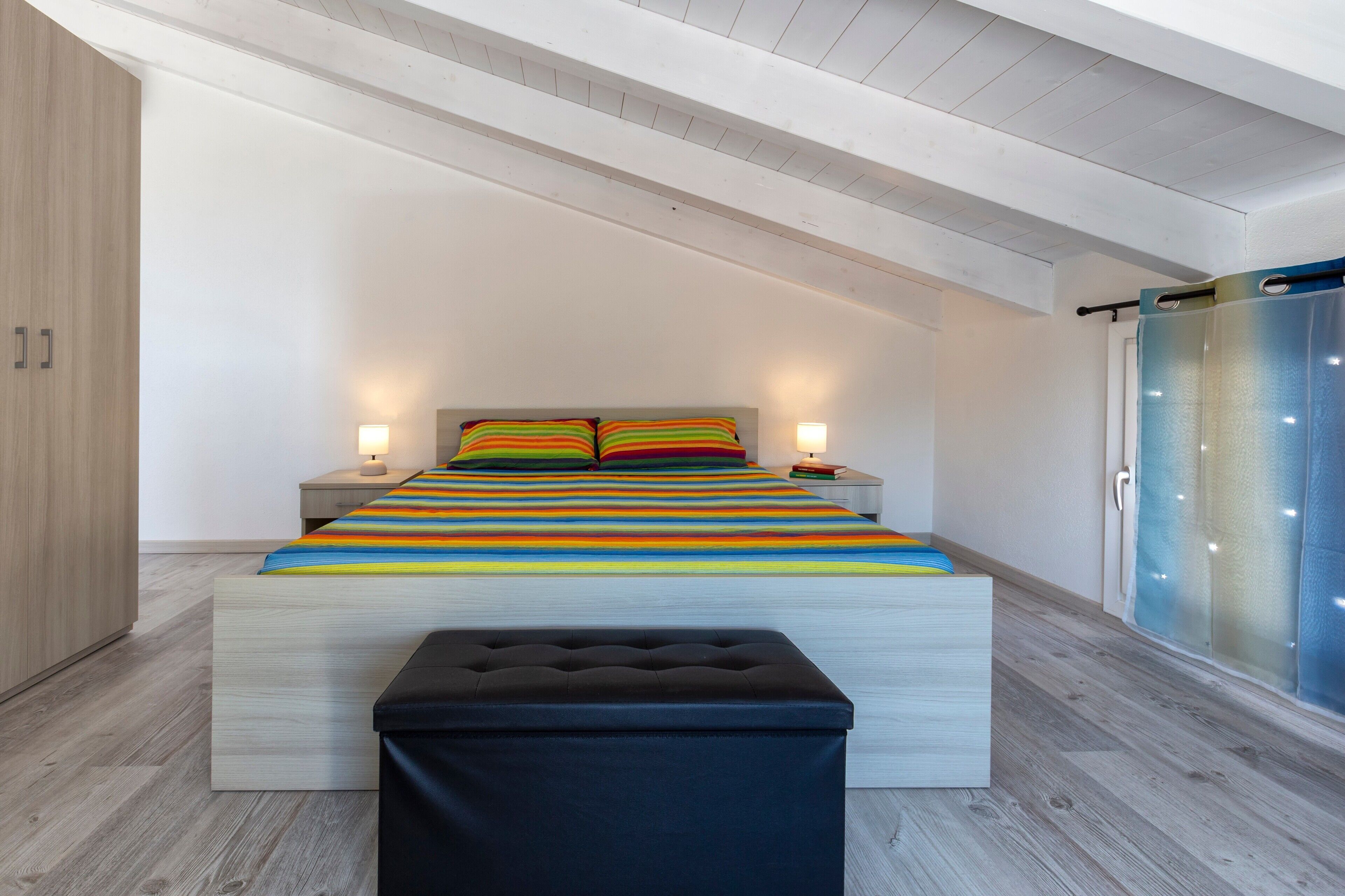 Un dormitorio con cama, lámparas de noche, mesita de noche, armario de madera y puerta de vidrio corredera.