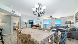 Un salon spacieux comprenant un coin repas, un ventilateur de plafond et une grande fenêtre donnant sur un paysage agréable.