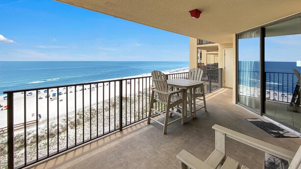 Un balcon avec vue sur la plage et l’océan, une table avec des chaises et une porte donnant sur une autre pièce.