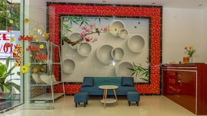 A modern hotel lobby with a blue sofa, a decorative wall with circular mirrors, and a reception desk. - Sala Hotel (Ho Chi Minh City)