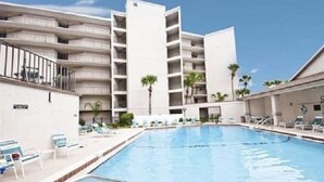 Ein modernes Hotel mit Pool, mehreren Balkonen und wolkenlosem, blauem Himmel.
