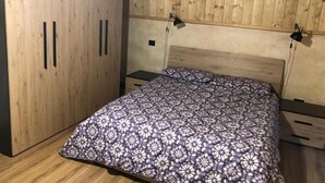 Ein Schlafzimmer mit Holzbalkendecke, einem Bett mit gemustertem Überwurf, einem zweitürigen Kleiderschrank und einem kleinen Nachttisch.