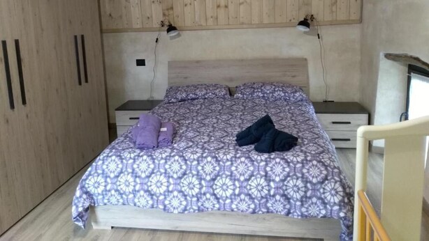 Ein Schlafzimmer mit Holzboden, einem Bett mit gemusterten Bettwaren, einem Nachttisch und einem Sessel.