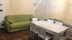 Ein Zimmer mit einem grünen Sofa, einem Holzesstisch und vier Stühlen sowie einer Stehlampe.
