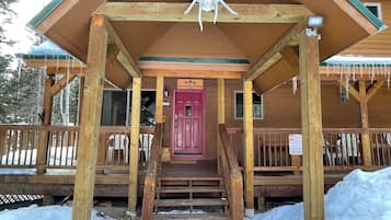 Una cabaña de madera con puerta roja, escalones de madera que conducen a la entrada y un letrero que indica prohibido estacionar por peligro.