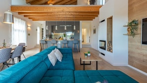 A spacious living area with a large teal sectional sofa, a wooden ceiling, and a kitchen in the background. - Villa Descansa (Nin)