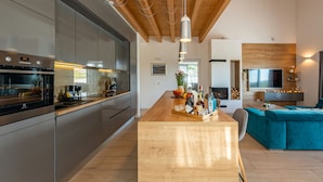 A modern kitchen with stainless steel appliances, a wooden island, and a teal sofa in a living area with a TV and fireplace. - Villa Descansa (Nin)