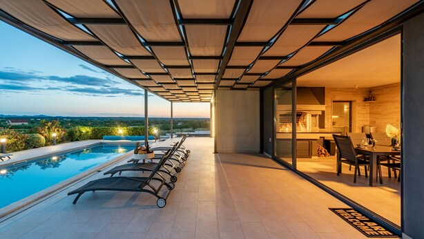 A modern outdoor pool area with lounge chairs and a dining table, overlooking a scenic landscape. - Villa Descansa (Nin)