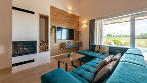 A modern living room with a large sectional sofa, a flat-screen TV, a fireplace, and a large window offering a view of the outdoors. - Villa Descansa (Nin)