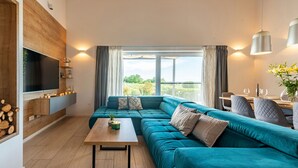 A modern living room with a teal sofa, a wooden coffee table, a flat-screen TV mounted on a wooden wall, and a dining area with a table and chairs. - Villa Descansa (Nin)