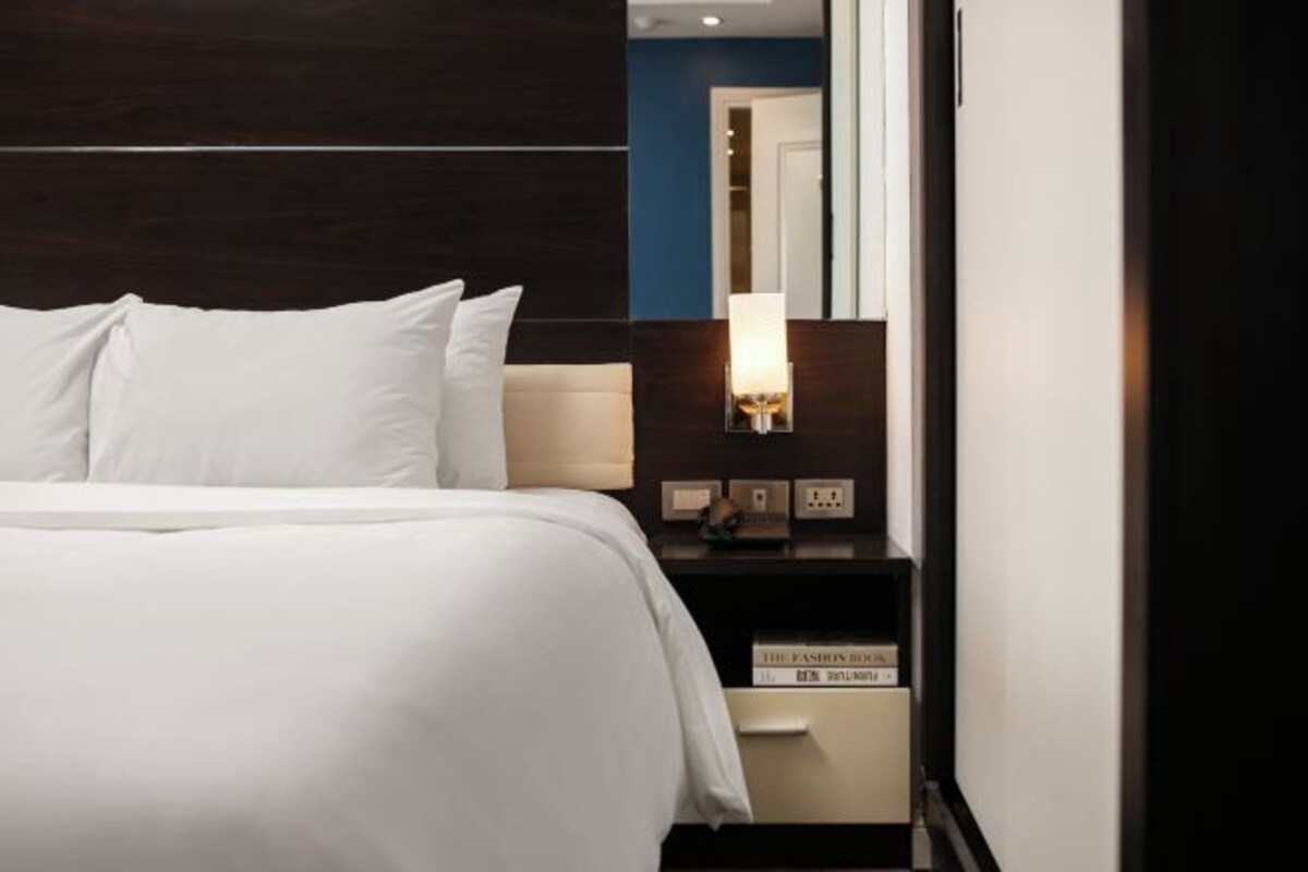A hotel room with a neatly made bed, a bedside table with a lamp, and a mirror.