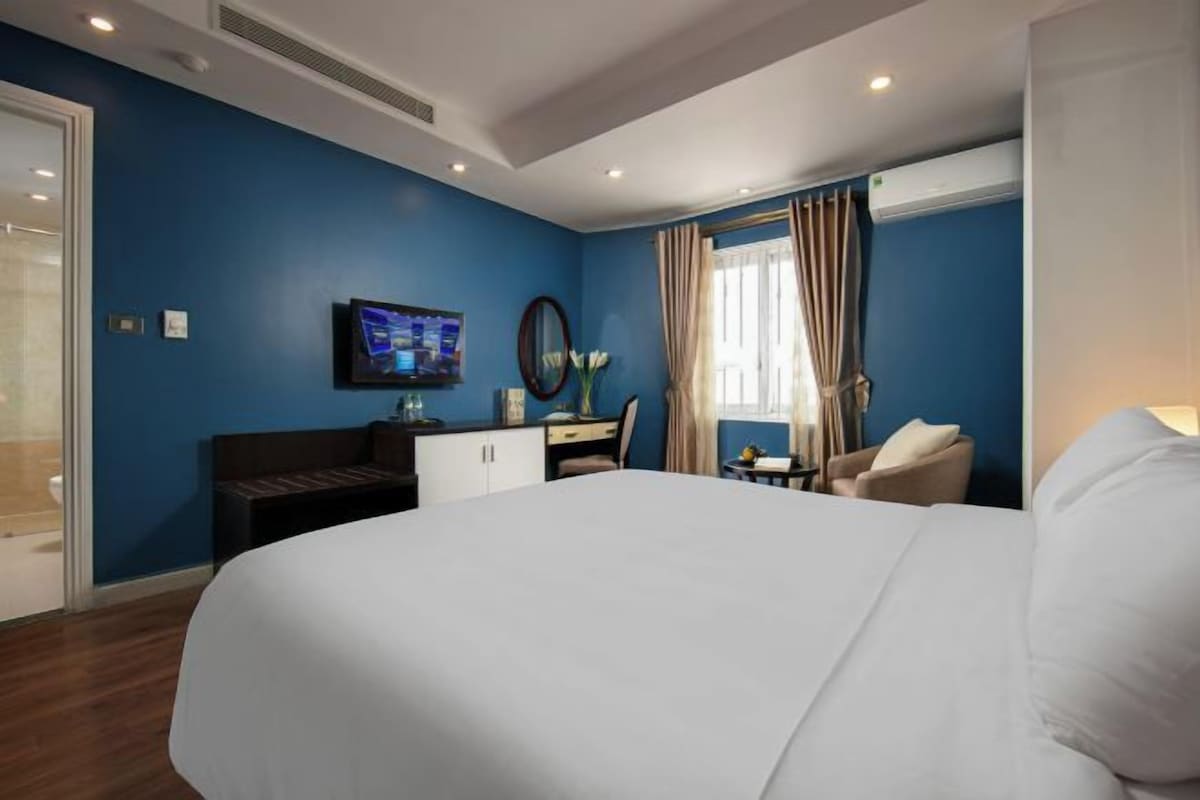 Une chambre d’hôtel avec un grand lit, un bureau, une chaise, une télévision et une fenêtre avec des rideaux.