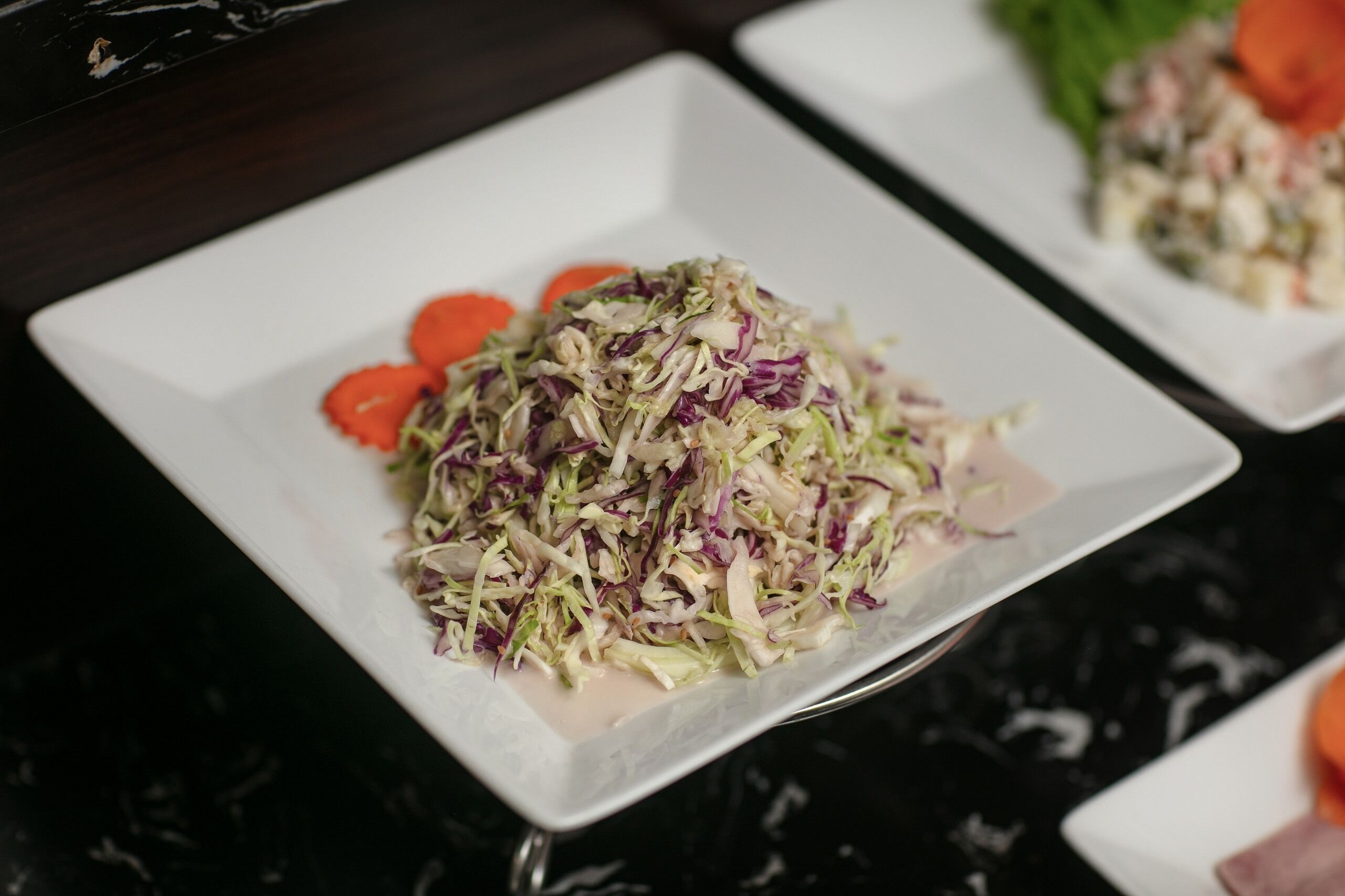 A white square plate with a salad on a dark marble table.