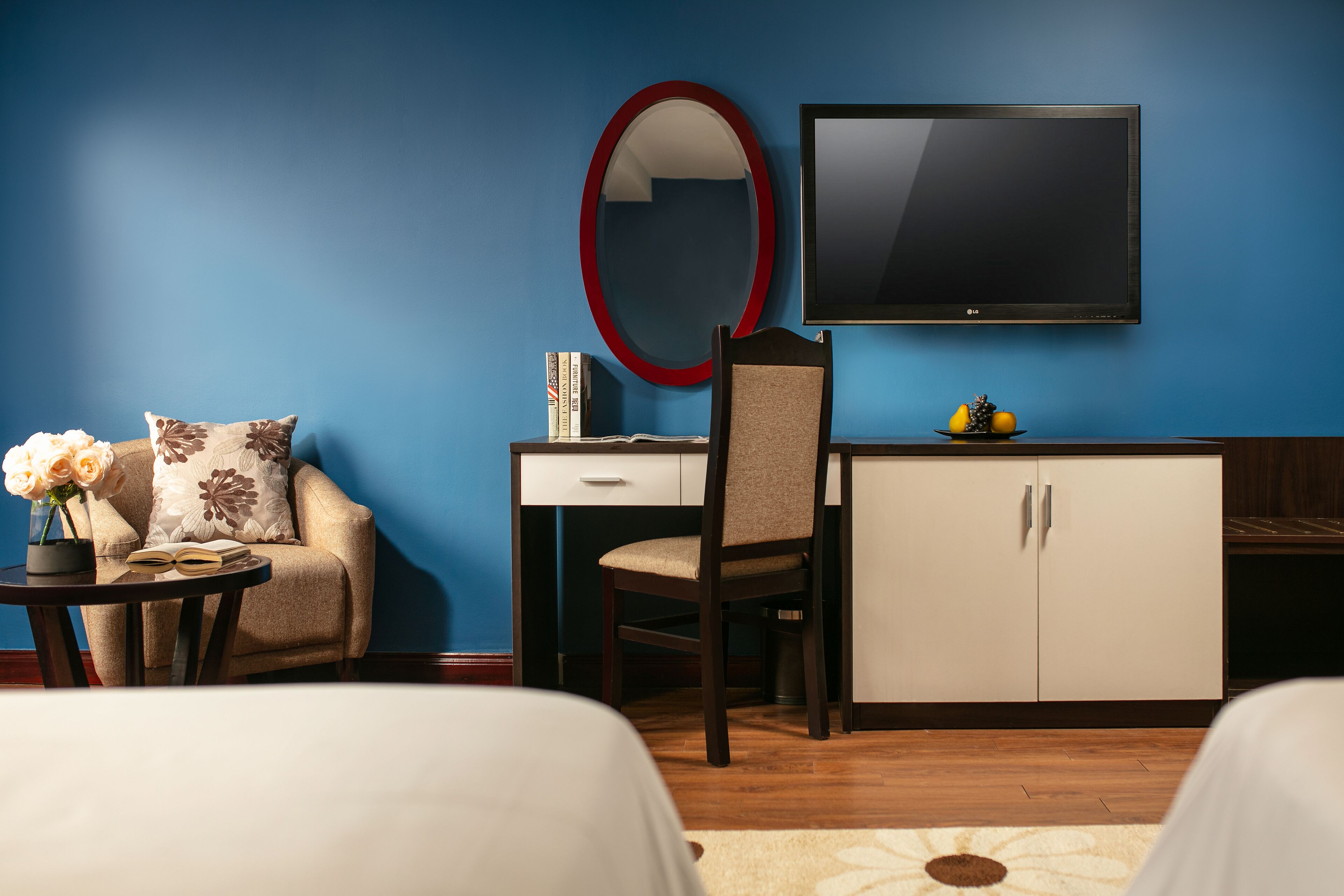 Una habitación de hotel con cama, escritorio con silla, televisor, armario y una pequeña mesa con un jarrón de flores.