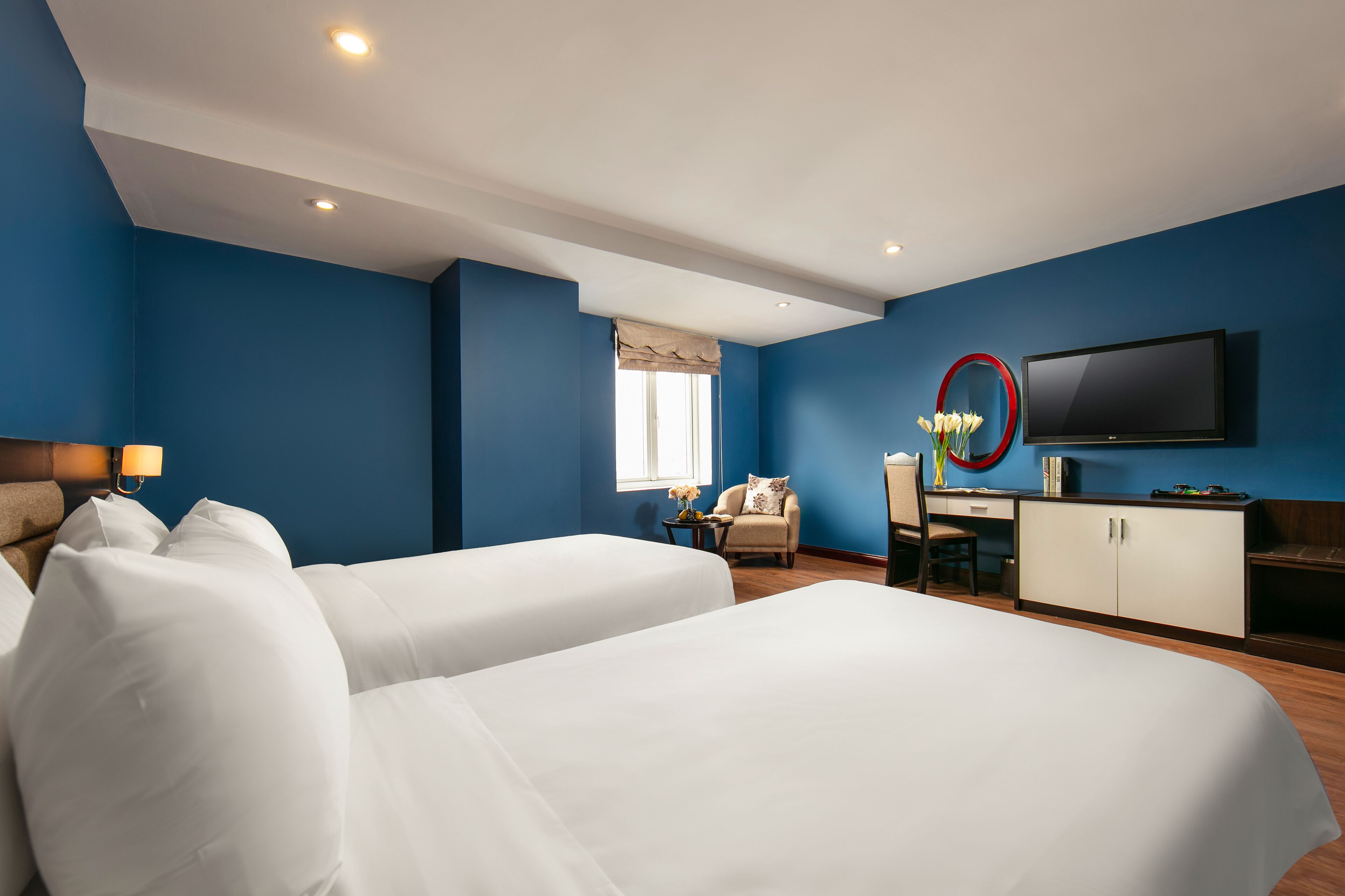 A hotel room with two beds, a desk, a chair, a TV, and a window with curtains.