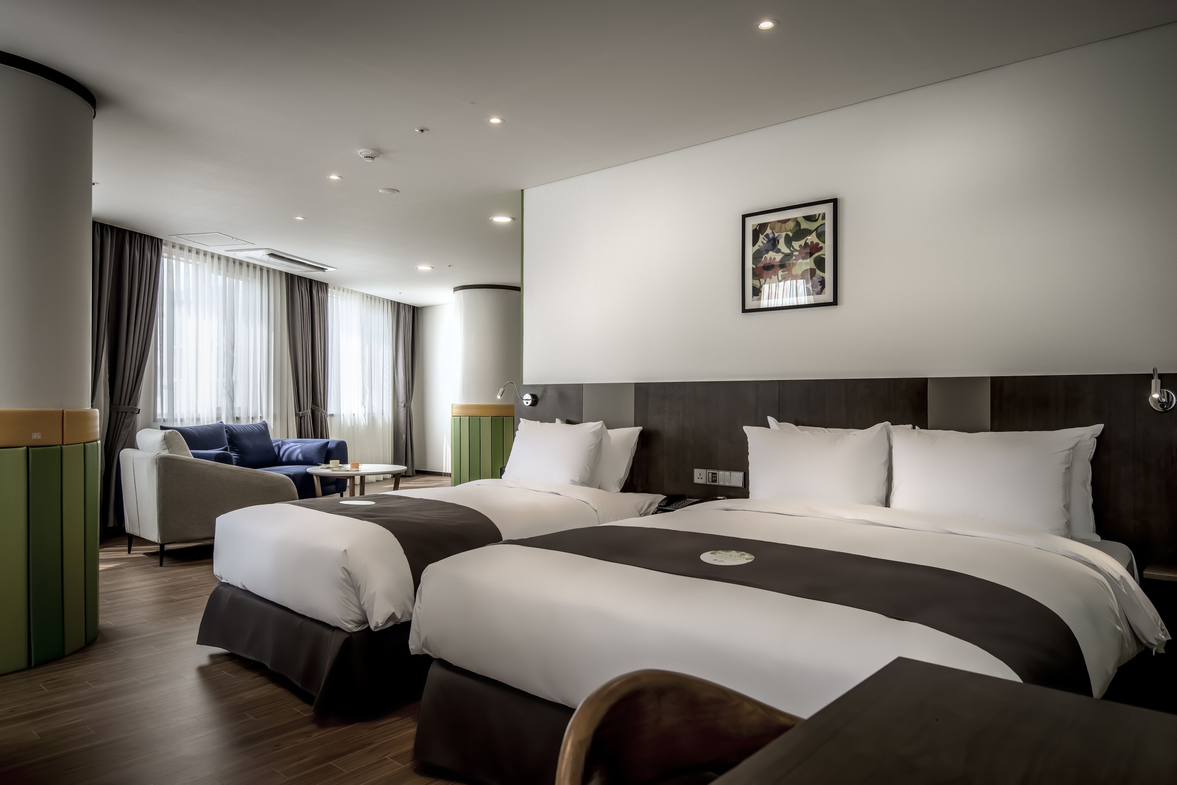 A hotel room with two beds, a sofa, a small table, and a green cabinet.