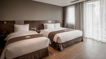 A hotel room with two beds, a wooden floor, a large window with curtains, and a modern headboard.