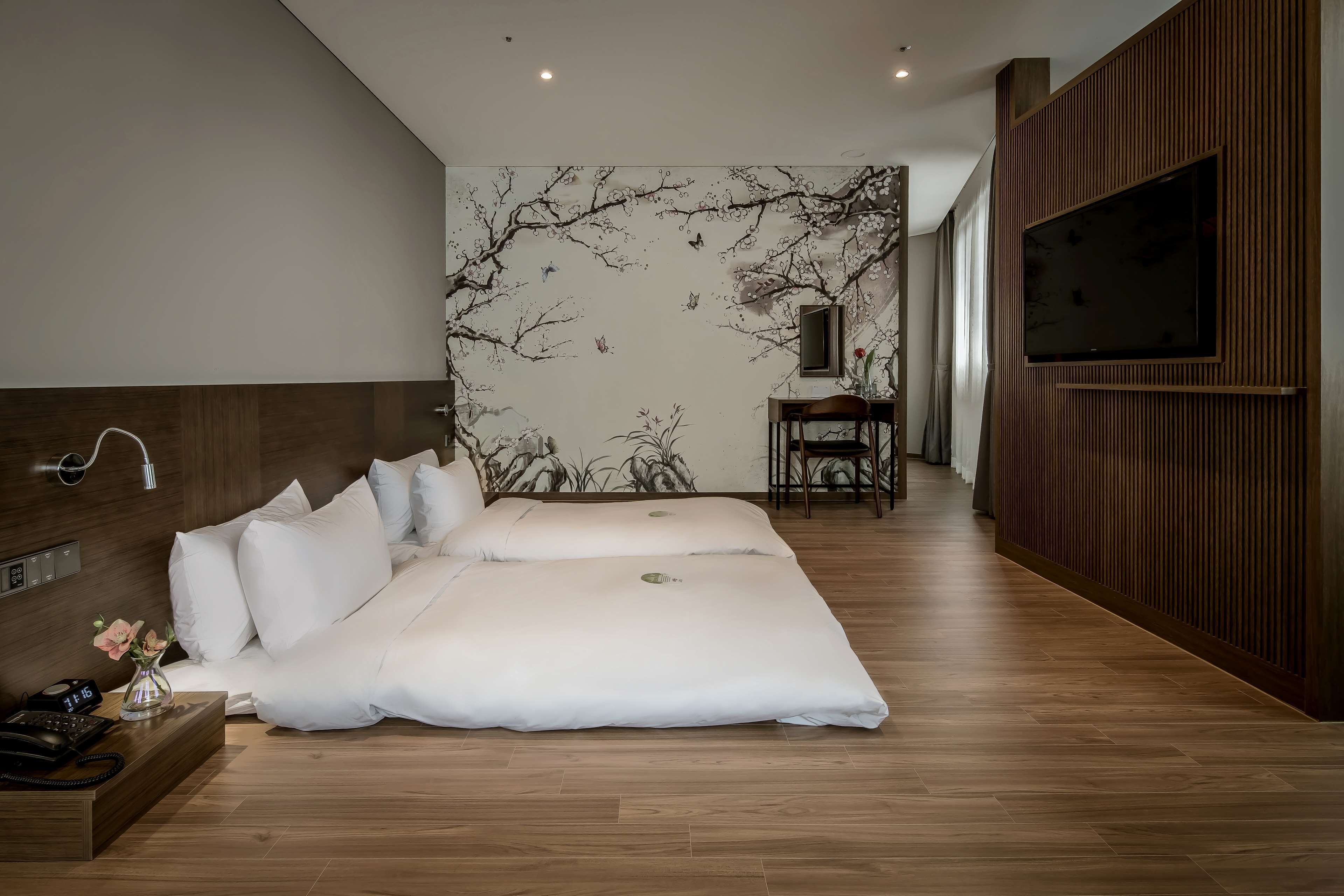 A modern hotel room with a large bed, a TV mounted on the wall, and a wooden panel design on one side.