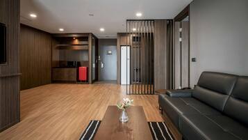 Una sala de estar moderna con un sofá de cuero negro, una mesa de centro de madera con un florero y una cocina con armarios de madera y un refrigerador rojo.
