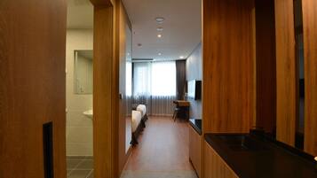 A hotel room with a wooden floor, a kitchenette, a bathroom with a toilet and sink, and a bed with a headboard.