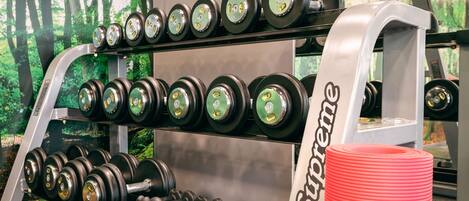 A weightlifting rack with various dumbbells and a red water bottle.