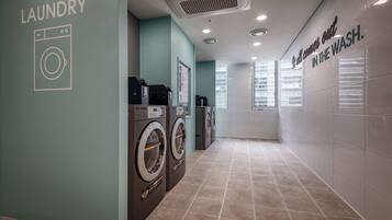 A laundry area with multiple washing machines, a wall-mounted dryer, and a sign that says "It all comes out in the wash."