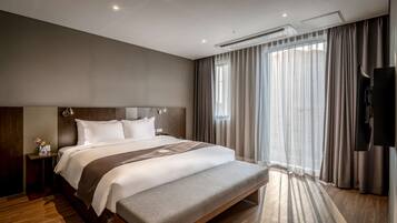 A modern hotel room with a large bed, a bedside table, a flat-screen TV, and a large window with curtains.