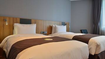A hotel room with two beds, wooden headboards, a nightstand, and a view of the city.