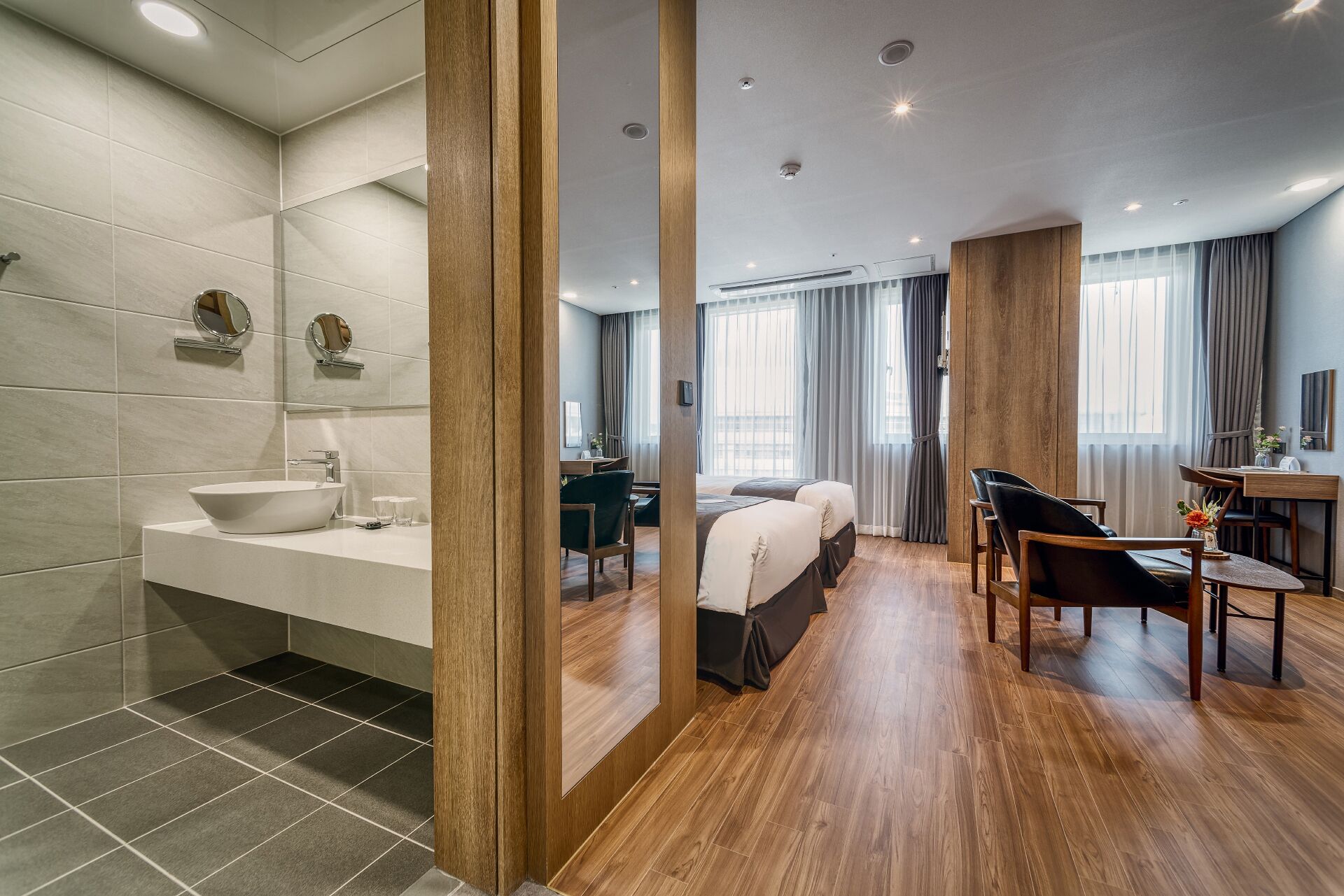 A modern hotel room with a bathroom, a sitting area with a table and chairs, and a bed.