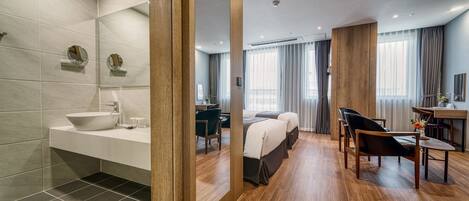 A modern hotel room with a bathroom, a sitting area with a table and chairs, and a bed.