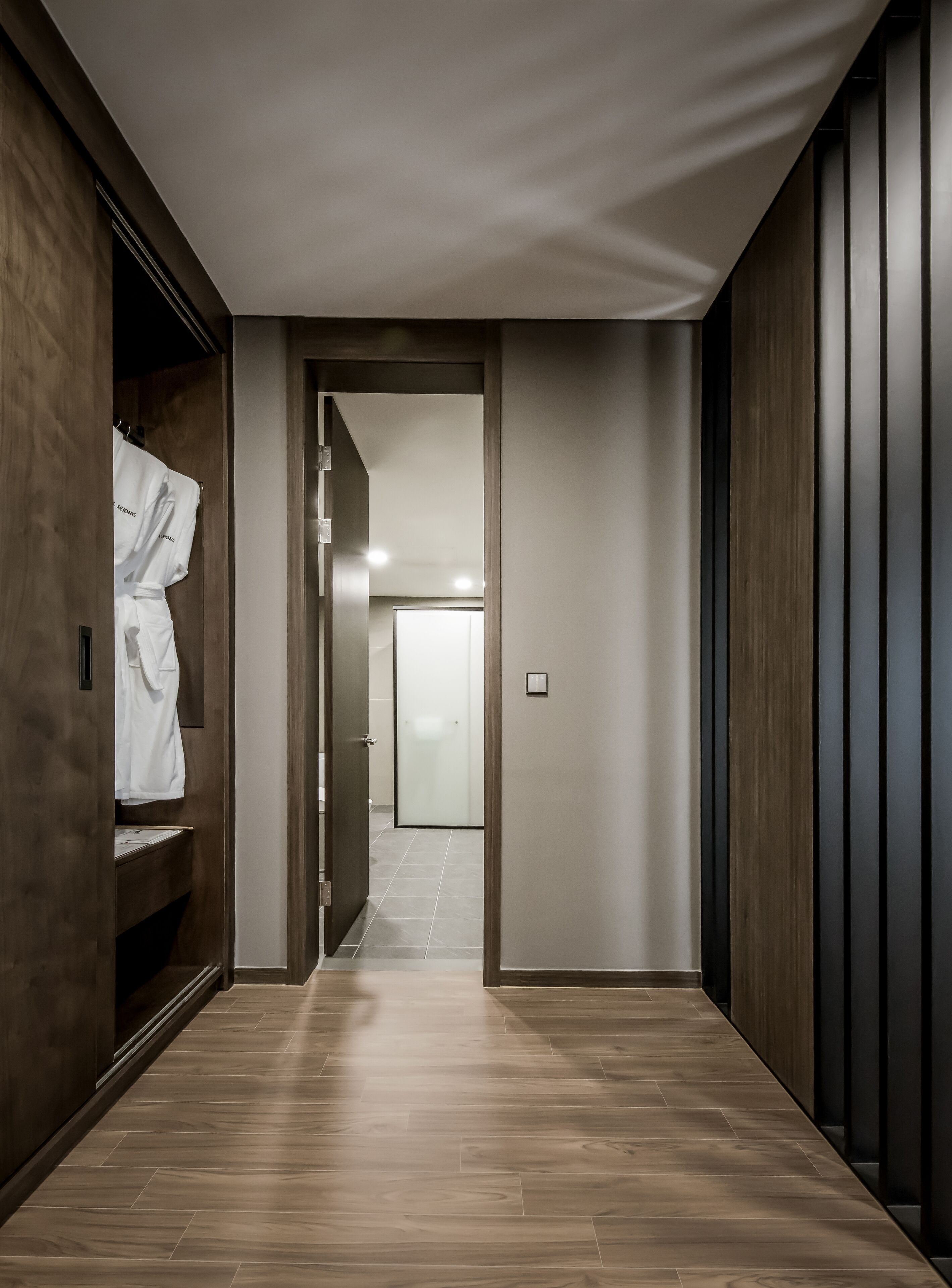 A hallway with wooden flooring and walls, leading to a room with a white door and a light fixture.