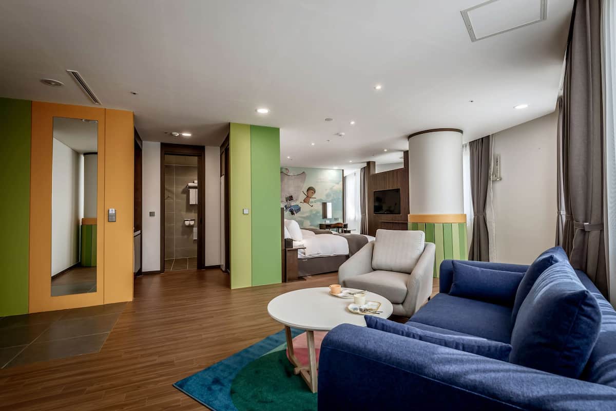 A modern hotel room with a blue sofa, a round table, and a bed with a view.
