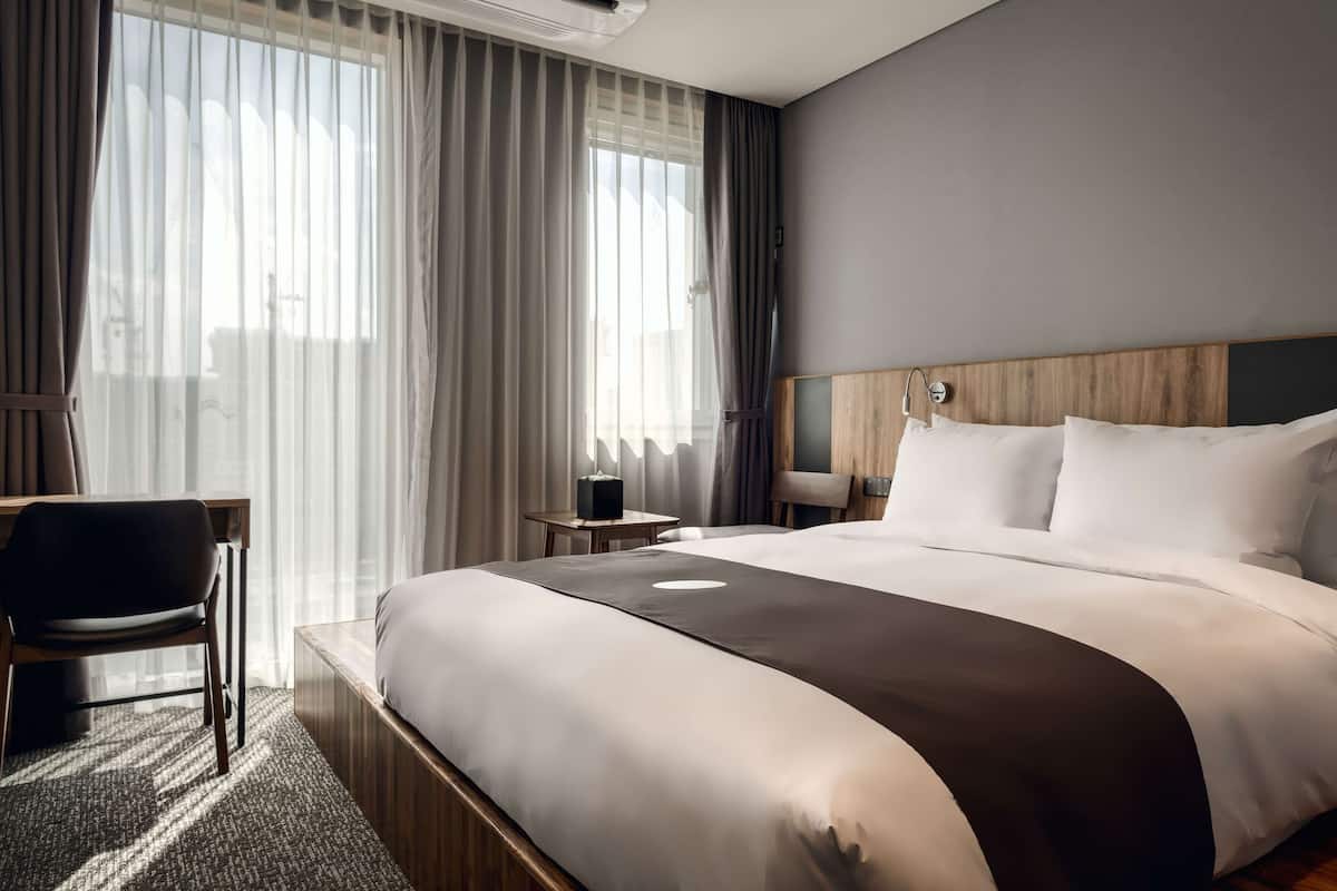 A hotel room with a large bed, a desk, a chair, and a small table.