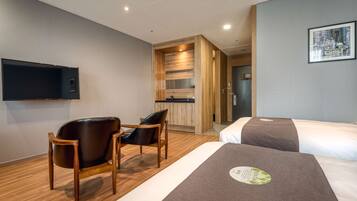 Une chambre d’hôtel avec deux lits, une chaise en bois, une petite table, un téléviseur à écran plat et une œuvre d’art représentant un paysage urbain accrochée au mur.