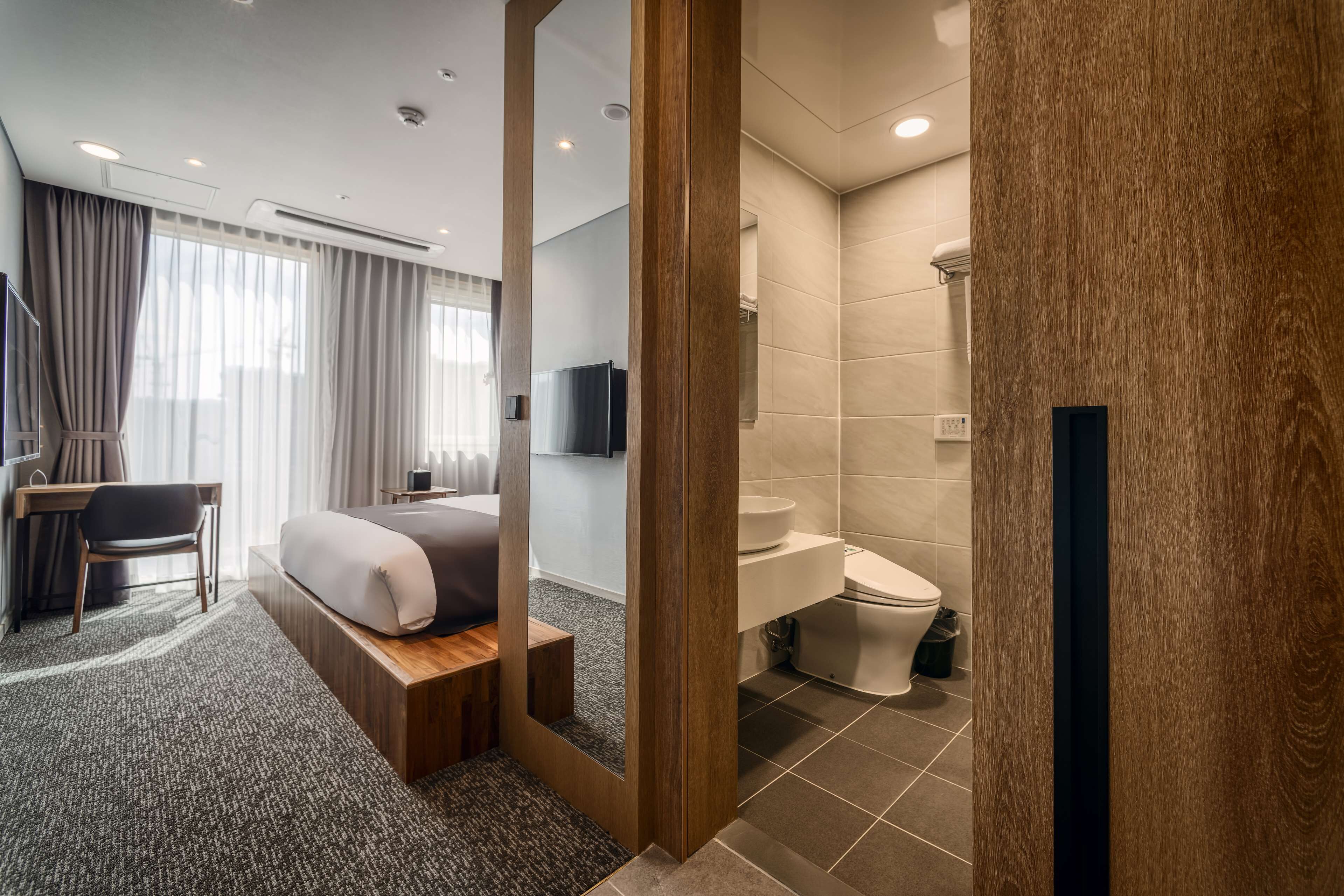 A modern hotel room with a bed, desk, and a large mirror.