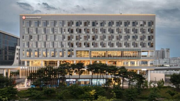 Un hotel moderno con una fachada de ventanas en forma de cuadrícula, una entrada destacada con puertas de vidrio y una terraza en la azotea.