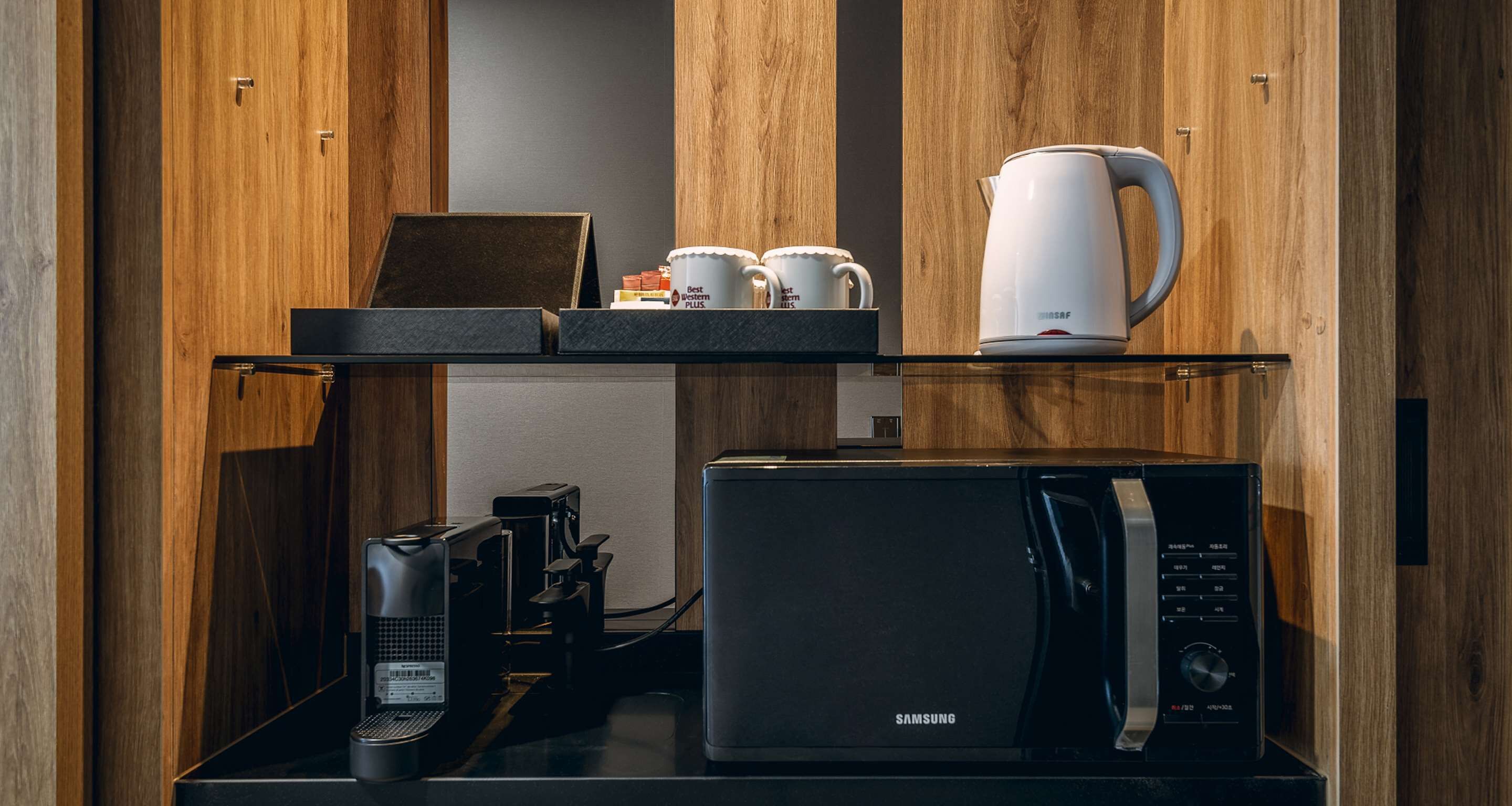 A kitchen area with a microwave, coffee maker, and a kettle on a shelf.