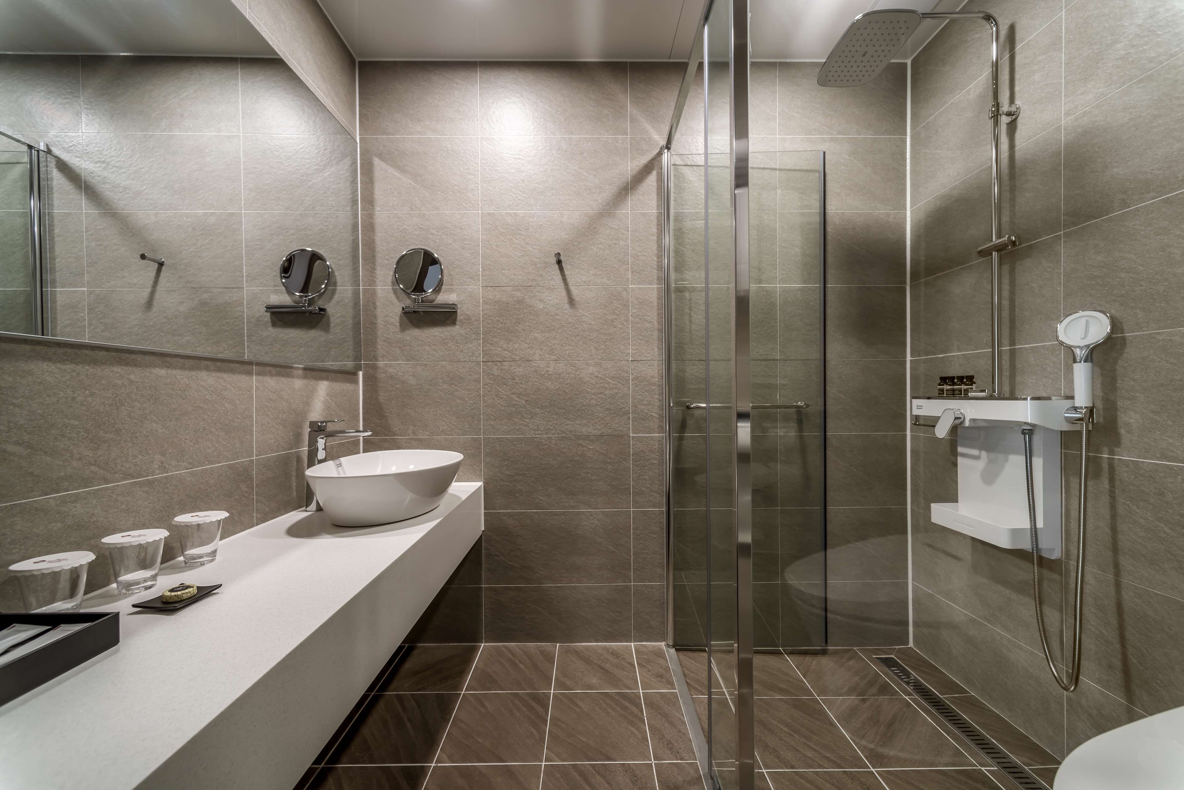 A modern bathroom with a glass-enclosed shower, a large white sink, and a vanity with a mirror and toiletries.