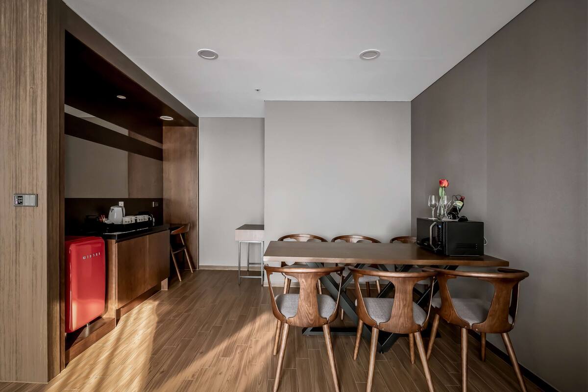 A modern dining area with a wooden table and chairs, a red refrigerator, and a kitchen area with a microwave.