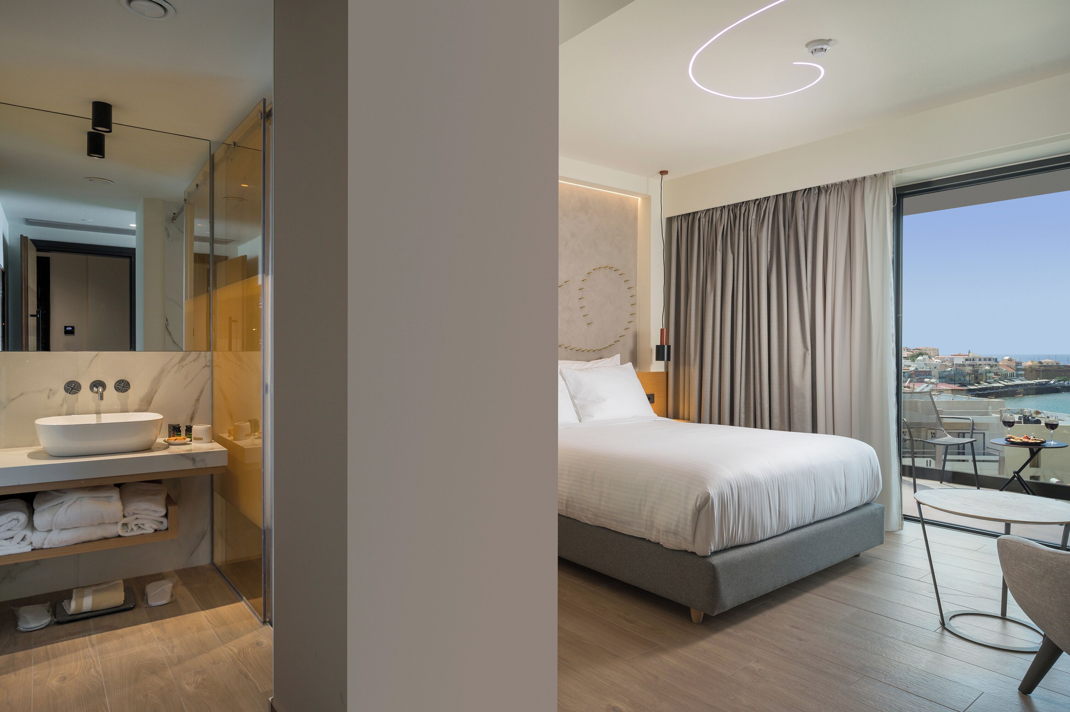 A modern hotel room with a large bed, a bathroom with a sink and towel rack, and a balcony with a view.