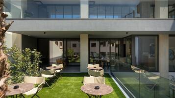 Un espace extérieur moderne aménagé avec des tables et des chaises, une rambarde en verre et une vue sur l’intérieur.