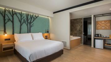 A modern hotel room with a large bed, a wall-mounted tree design, a small kitchen area, and a separate bathroom.