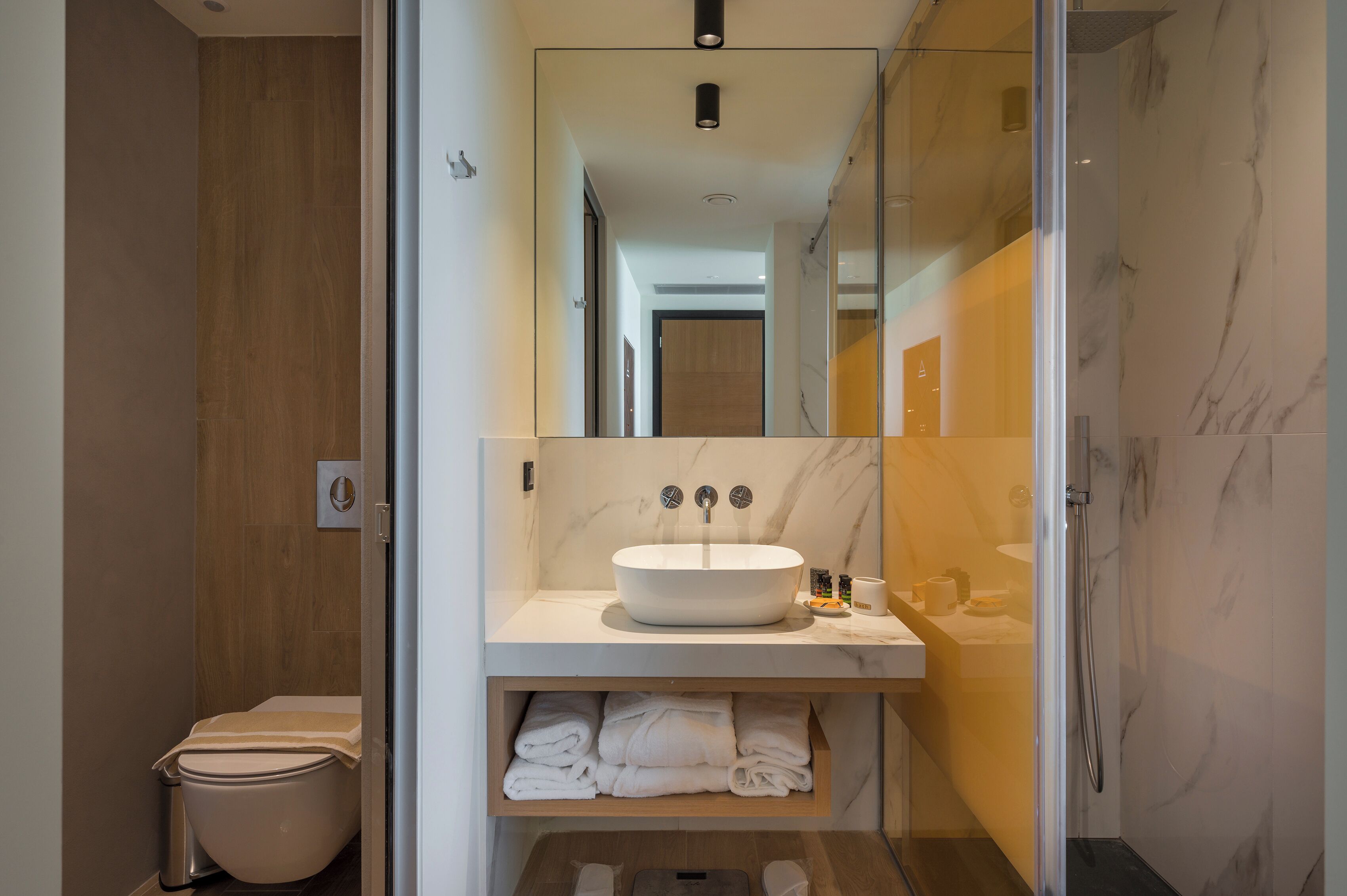 Une salle de bain moderne avec un lavabo blanc, des murs en marbre et une douche à parois de verre.