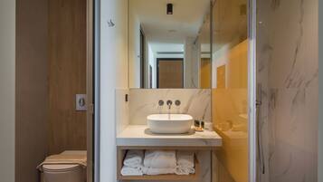 A modern bathroom with a white sink, marble walls, and a glass shower enclosure.