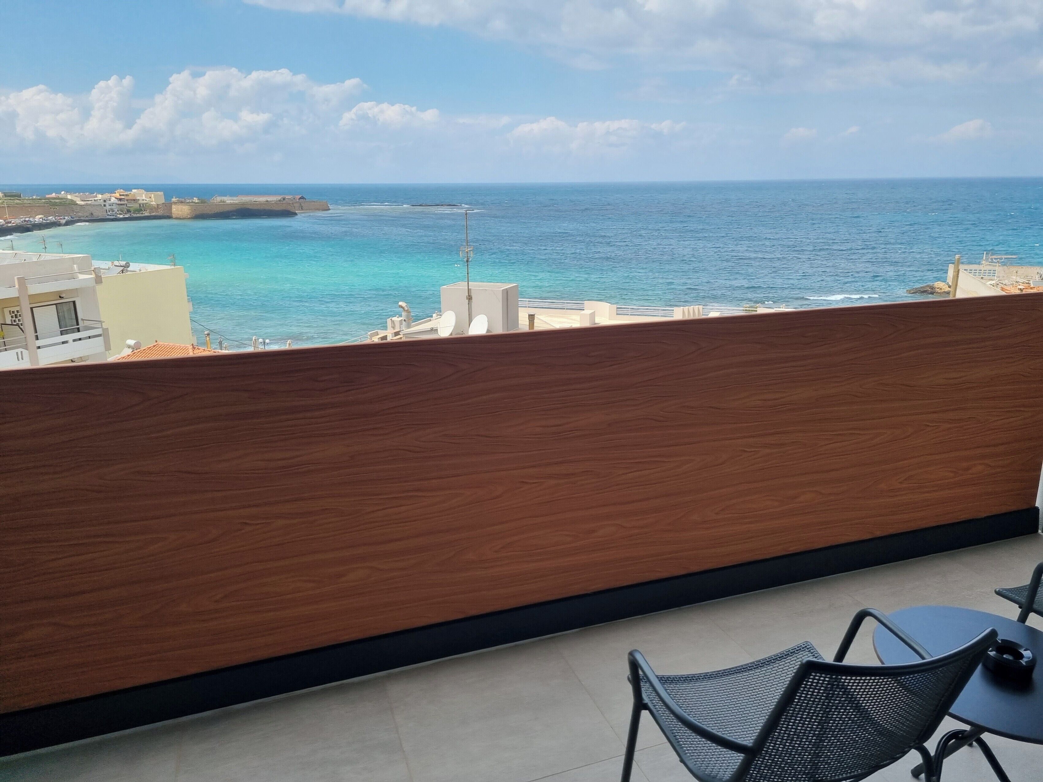 A balcony with a view of the sea, a table, and two chairs.