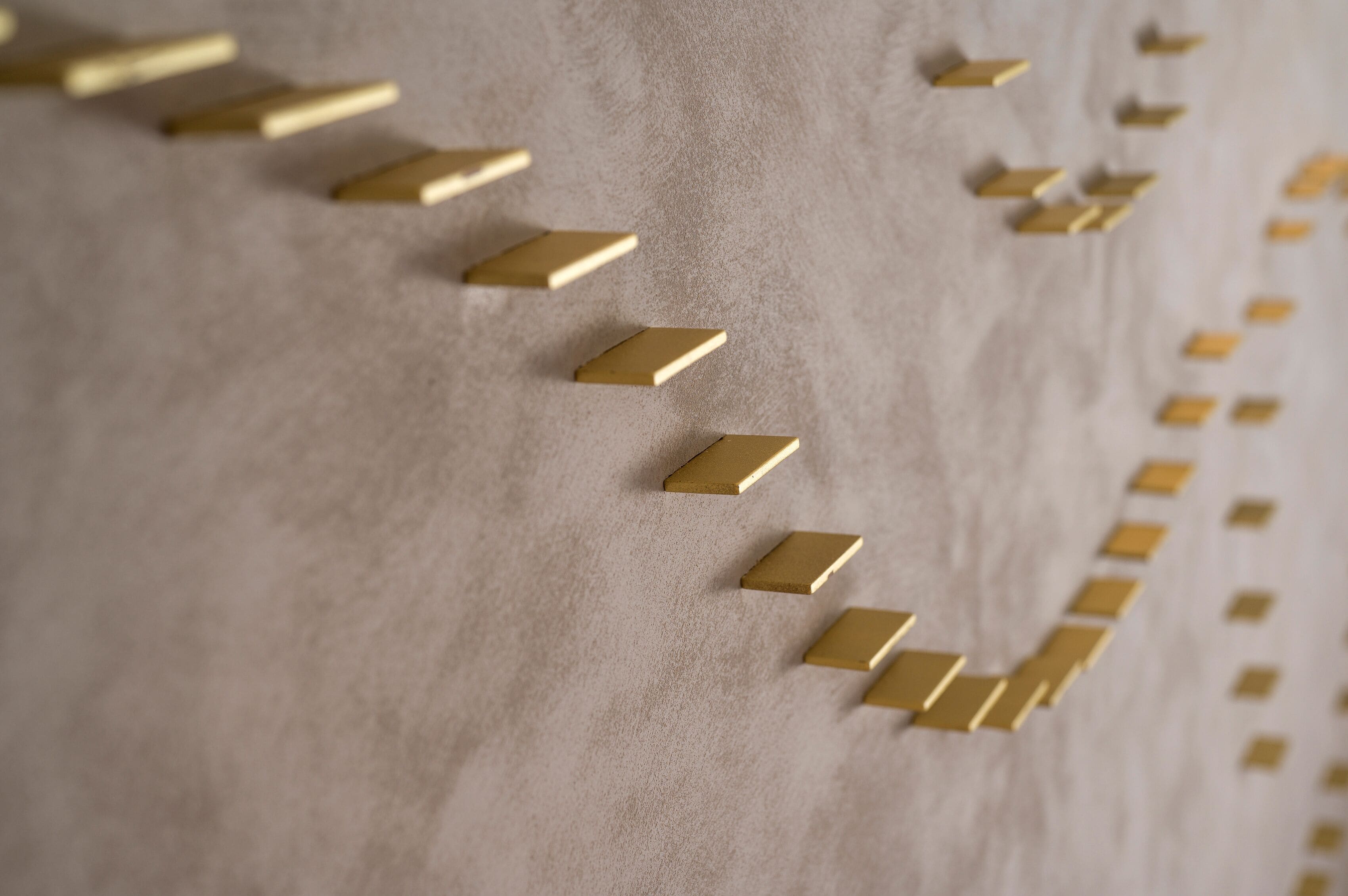A close-up of a textured surface with a pattern of gold-colored, rectangular shapes arranged in a diagonal line.