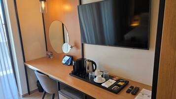 Habitación de hotel con un escritorio de madera, televisor, cafetera y una bandeja con tazas y un control remoto.