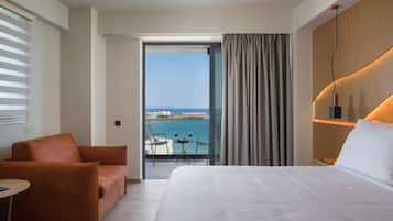 A hotel room with a large bed, a sofa, a balcony with a table and chairs, and a view of the sea.