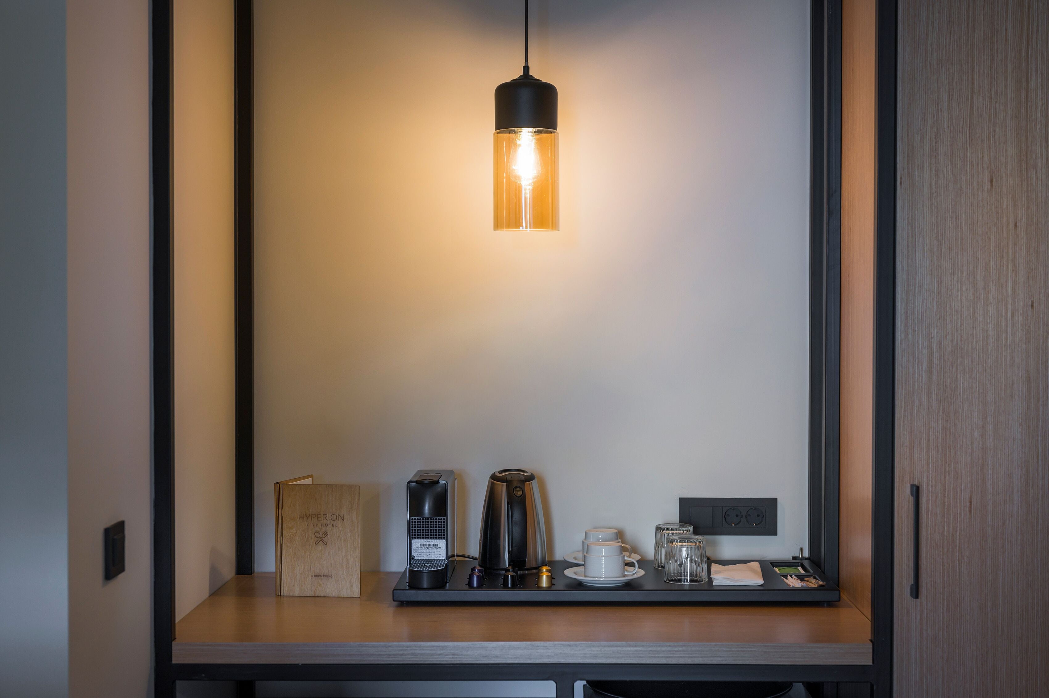 A minimalist room with a wooden desk, a coffee maker, a cup, and a small book.