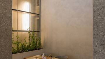 Un rincón comedor con mesa y sillas de madera, un separador de vidrio esmerilado y una maceta con plantas verdes.